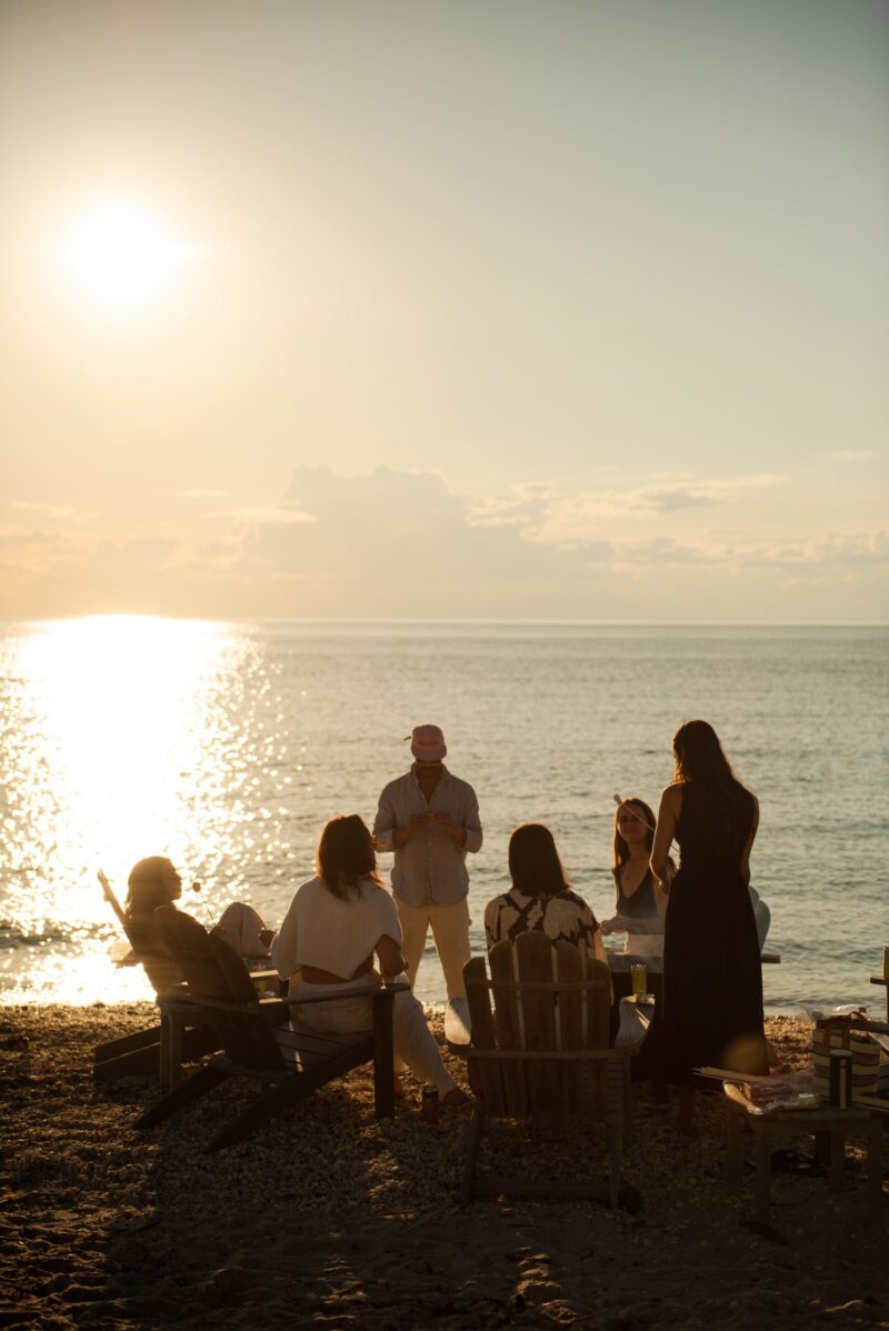 A group of people gathered at the beach at sunset.