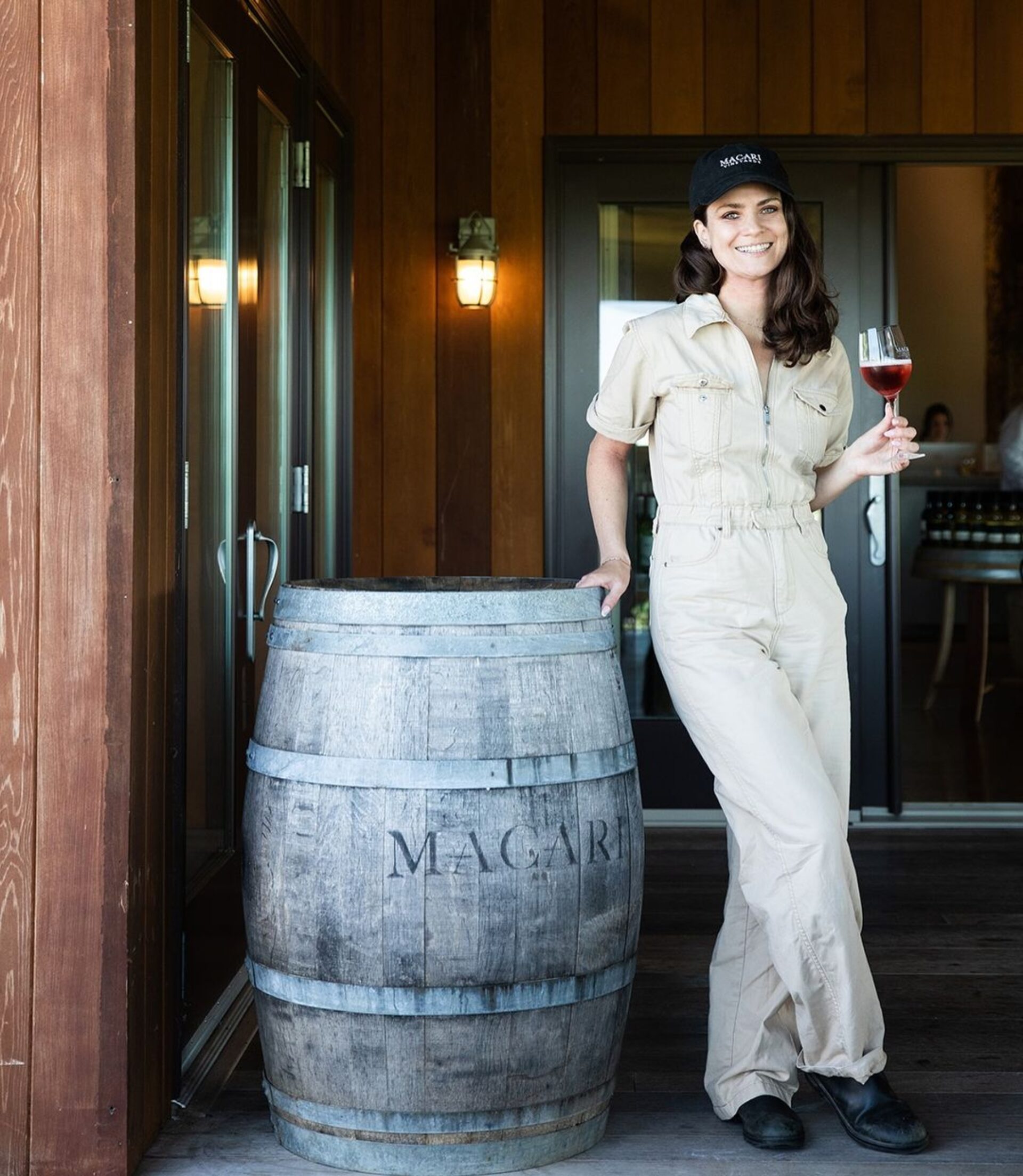 A woman with a wine glass, leaning up against a barrel of wine.