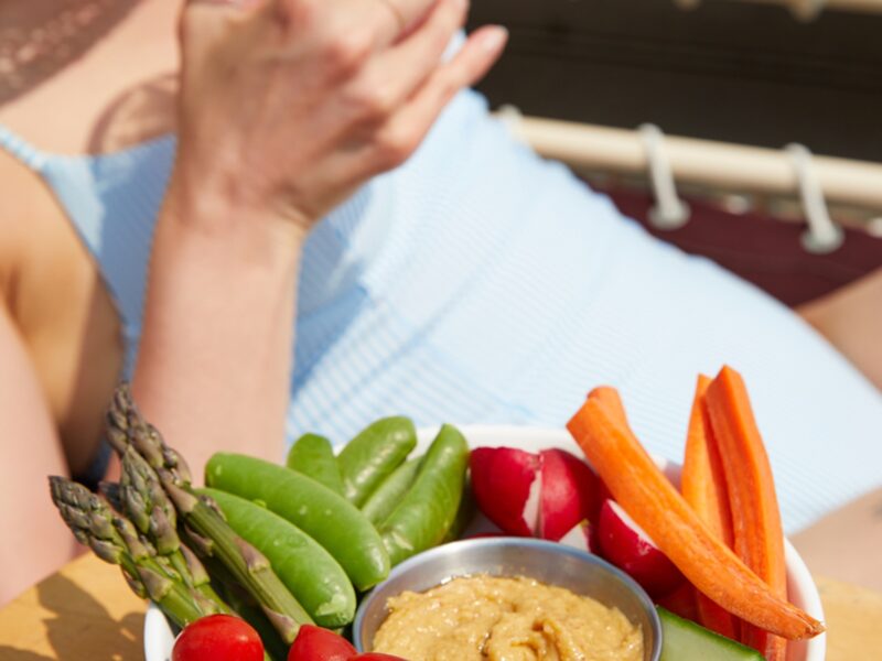 A woman in a blue swimsuit enjoying crudite and hummus.