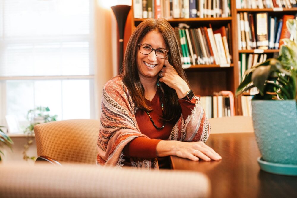 Therapist Lisa C. DeLuca posing for a headshot in her office, surrounded by books.