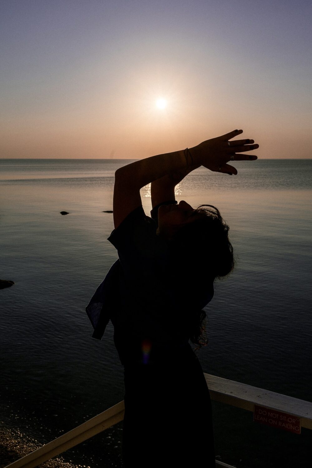 A woman practicing yoga outside, with the sun setting in the background.