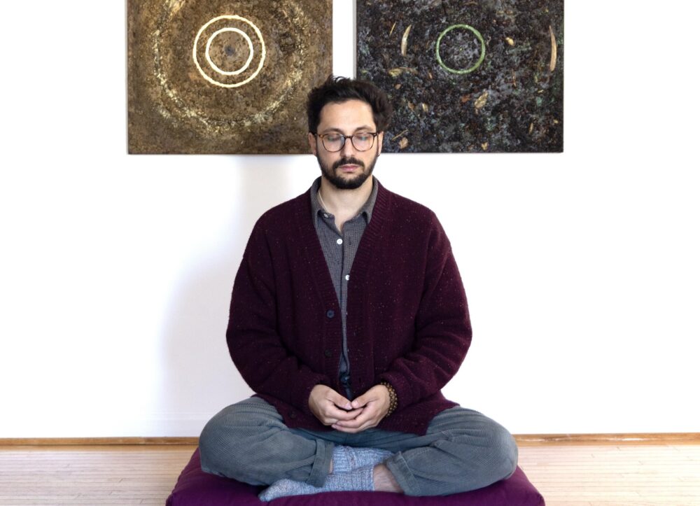 A man meditating on a purple cushion.
