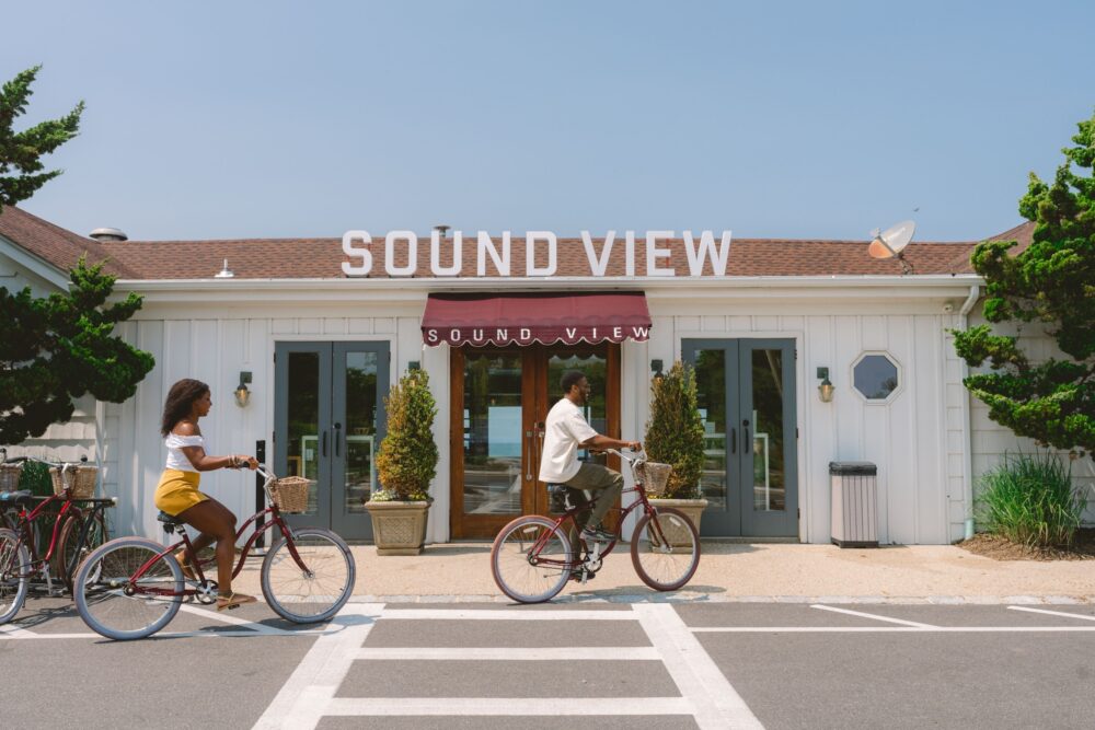 A couple riding complimentary bikes by the entrance of Sound View Greenport.