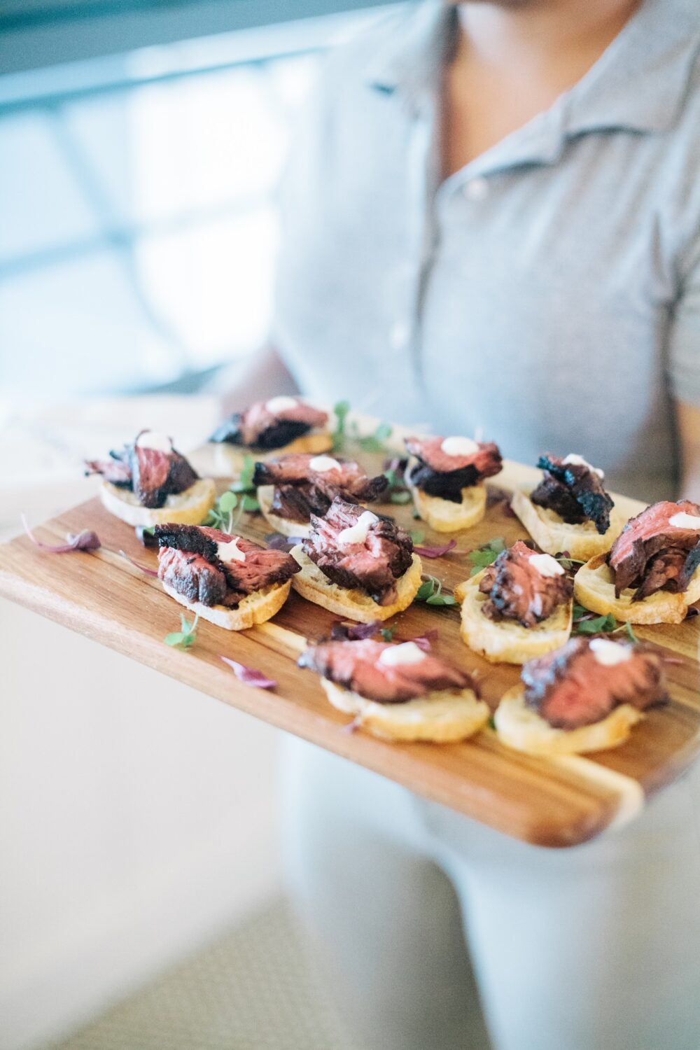 A platter of steak crostini appetizers on a wood board.
