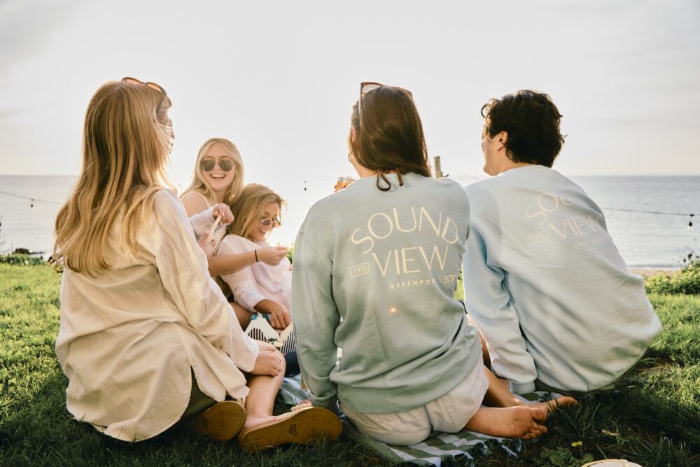 Friends sitting on grass, overlooking the beach at Sound View Greenport.
