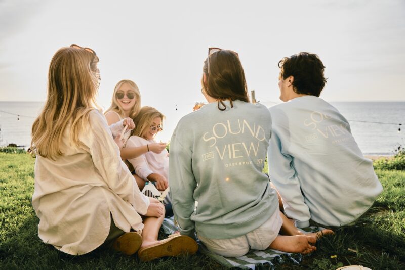 Friends sitting on grass, overlooking the beach at Sound View Greenport.