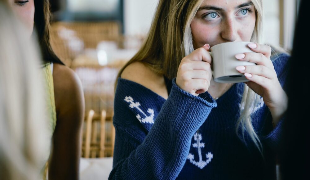 A woman in a navy sweater drinking a cup of coffee.