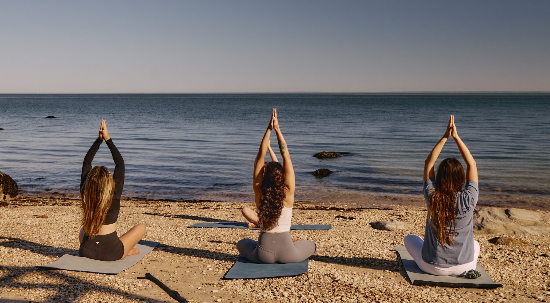 Three women practicing yoga on the beach in North Fork.