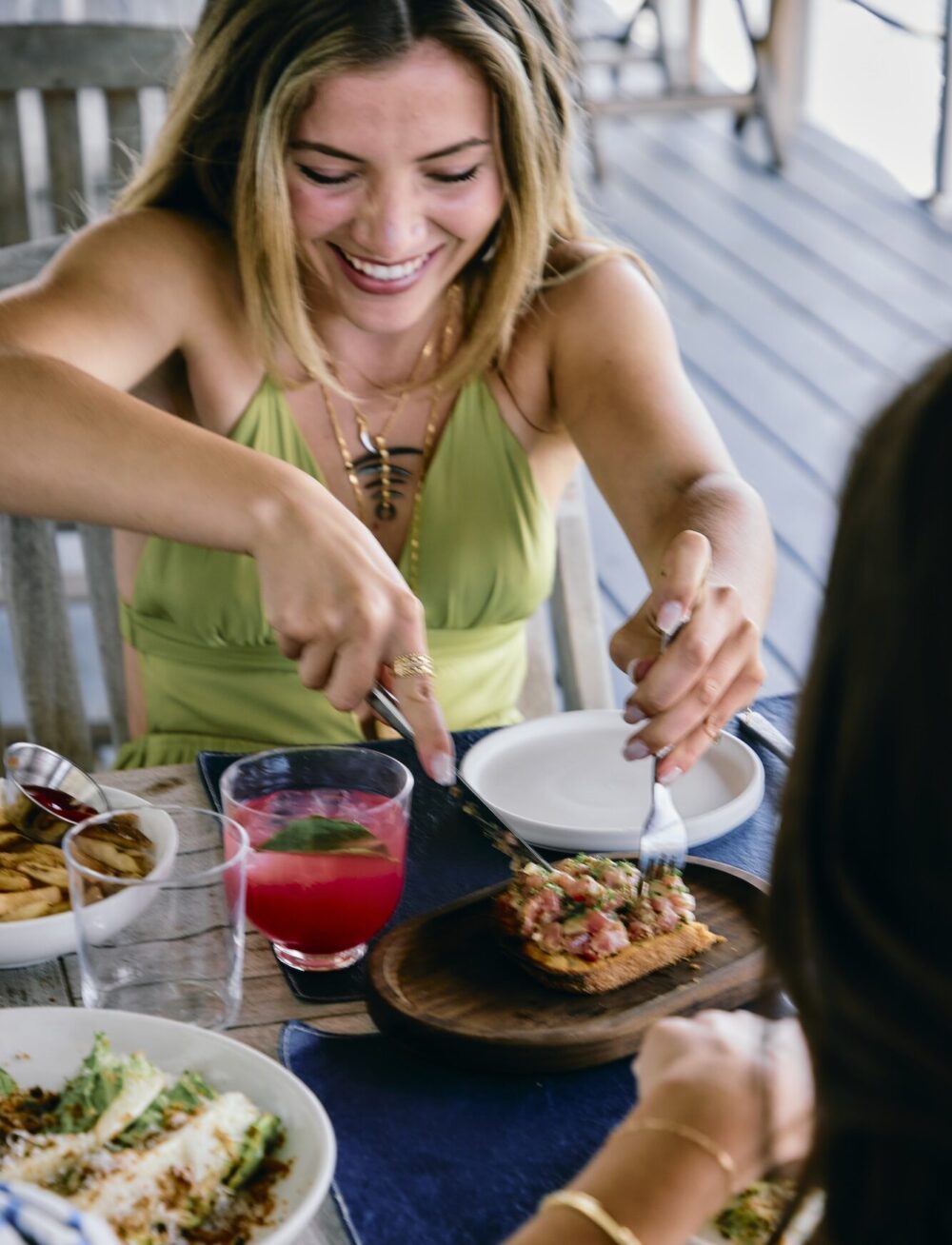 A woman having cocktails and cutting a tuna tartare appetizer.