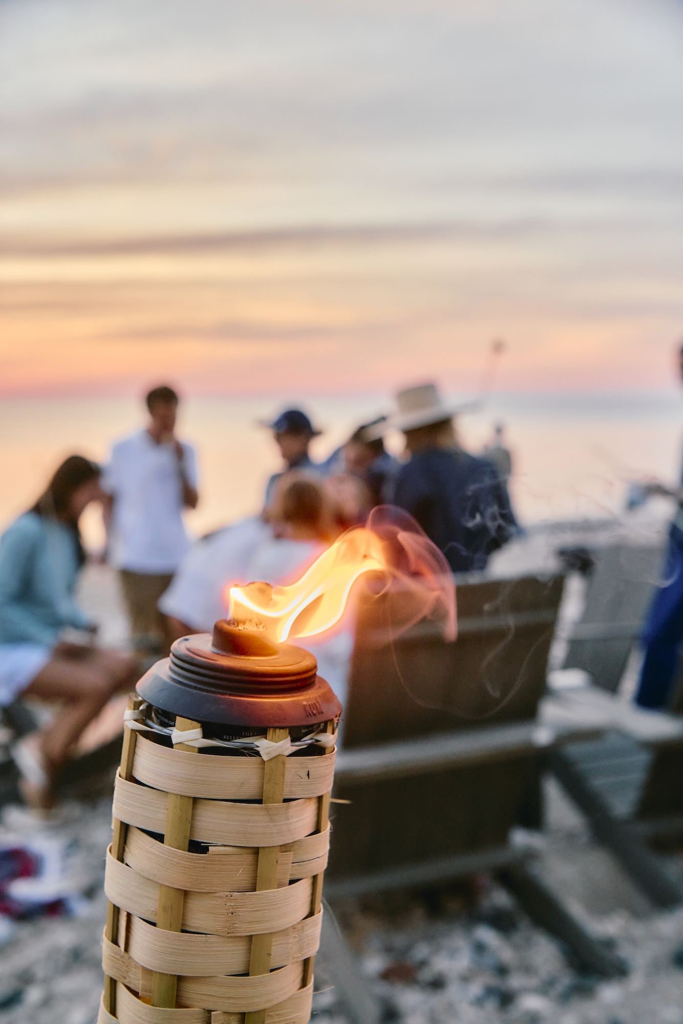 A tiki torch and a group of people gathered at the beach.