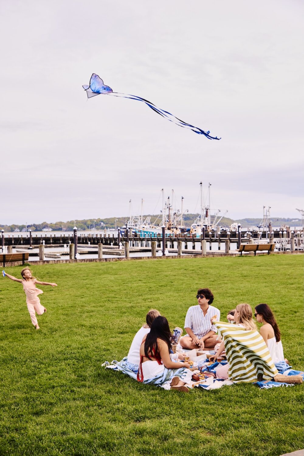 A kid playing with a kite in a park, and a group having a picnic.