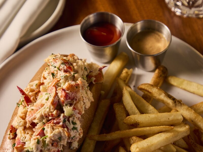 A lobster roll with fries and sauces.