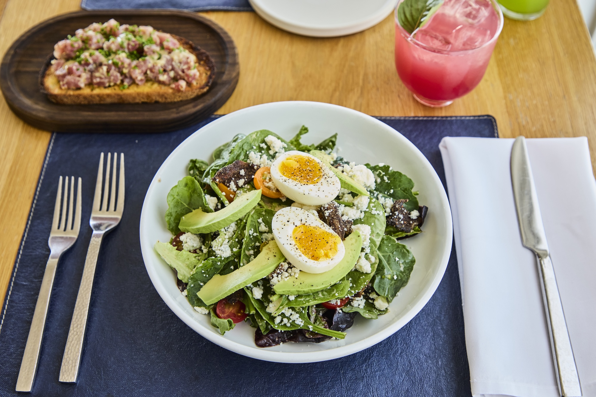 A green salad with hard boiled eggs, tuna tartare appetizer and cocktail.