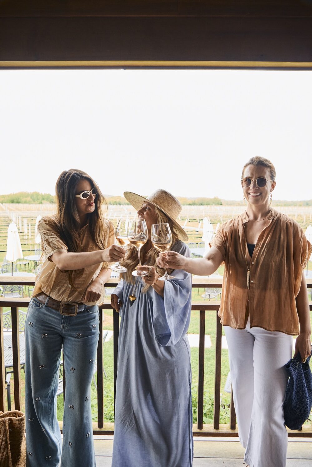 Three friends toast wine glasses at a vineyard.