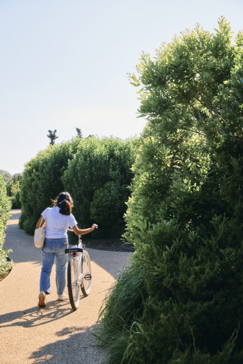 A woman walking alongside a bike on a path by Sound View Greenport.