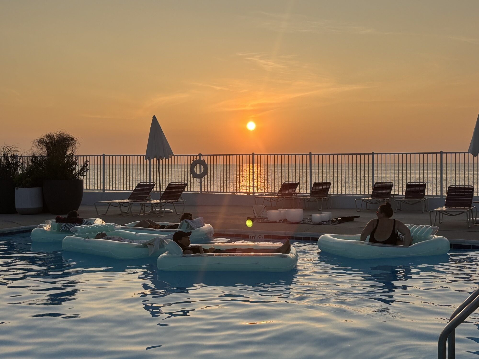 People floating in the pool at sunset for a sound bath.
